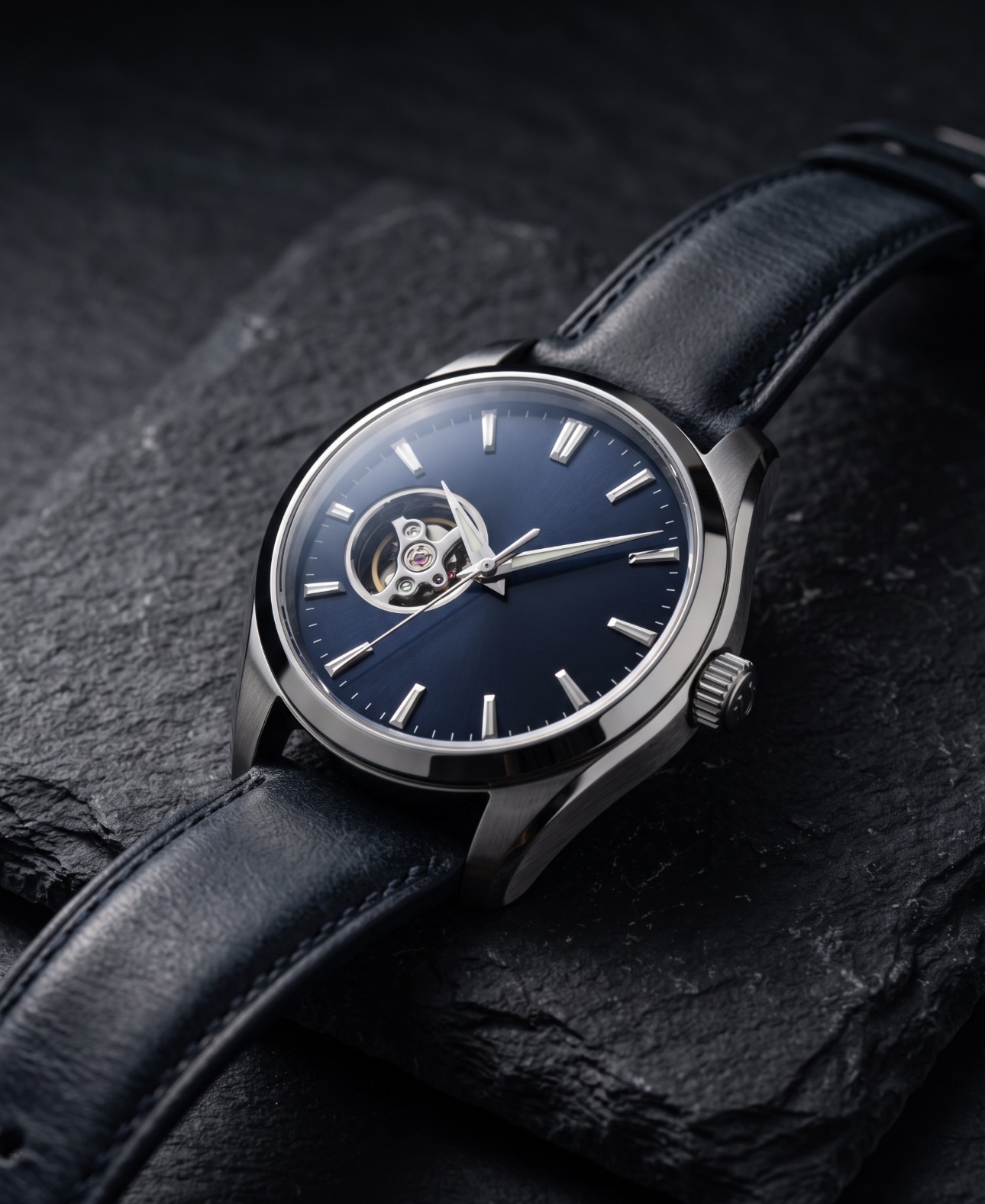 A luxury wristwatch with blue dial on dark slate, studio lighting